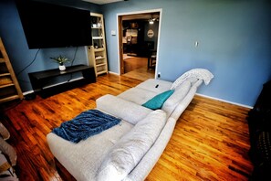 Una sala de estar con sofá, televisión y piso de madera.