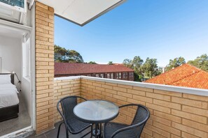 A balcony with a table and chairs, a brick wall, and a view of a red-roofed building. - Rooftop-Pool Studio Stay in Bondi (Bondi)