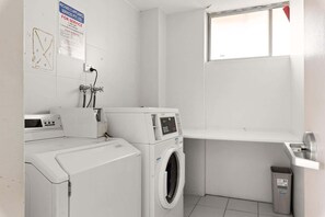 A laundry room with a washing machine, dryer, and a small window. - Rooftop-Pool Studio Stay in Bondi (Bondi)