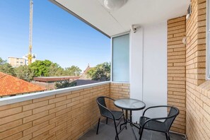 A balcony with two chairs and a table, a brick wall, and a view of buildings and trees. - Rooftop-Pool Studio Stay in Bondi (Bondi)