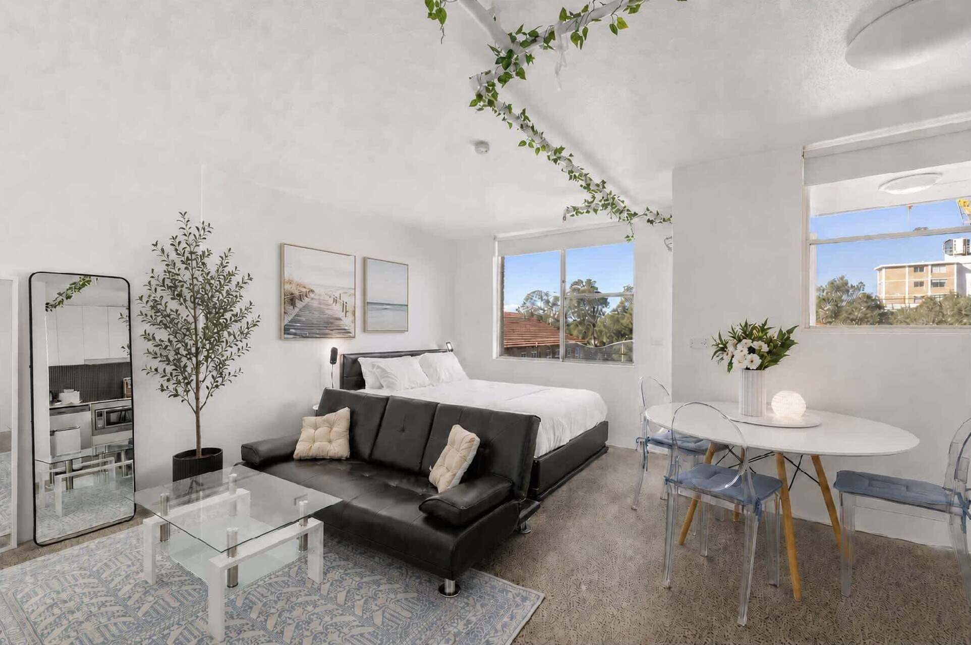 Ein modernes Schlafzimmer mit einem Bett, einem Glastisch, einer Couch, einem Esstisch mit Stühlen und einem großen Fenster.
