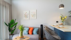 Un salón moderno con un sofá, una mesa de centro, una planta grande y una pequeña cocina con una barra.