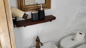 A bathroom with a gold-framed mirror, a white sink, a toilet, and a shelf with toiletries. - Room-charming Studio Rental in Mikonos w (Mykonos)