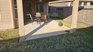 A covered patio with a table and chairs, a ceiling fan, and a wooden fence in the background. - Peaceful Retreat for Travel Nurses & Corporate Stays (Spring)