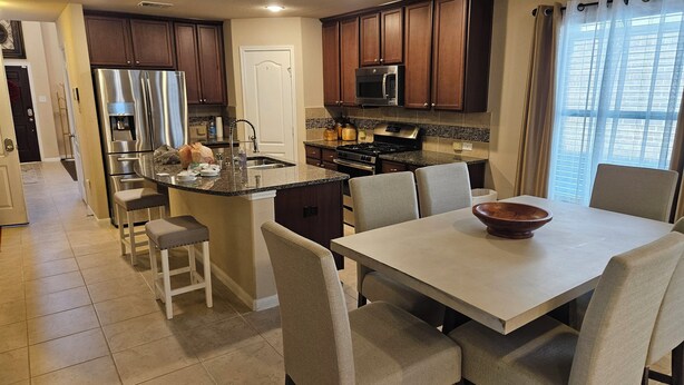 A modern kitchen with a central island, bar stools, a dining table with chairs, and a view of the outdoors. - Peaceful Retreat for Travel Nurses & Corporate Stays (Spring)