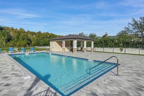 Ein rechteckiger Pool mit Fliesen, einer überdachten Laube und blauen Liegestühlen.