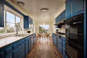 Eine moderne Küche mit blauen Schränken, Holzboden, einer Essecke mit Stühlen und einem großen Fenster.