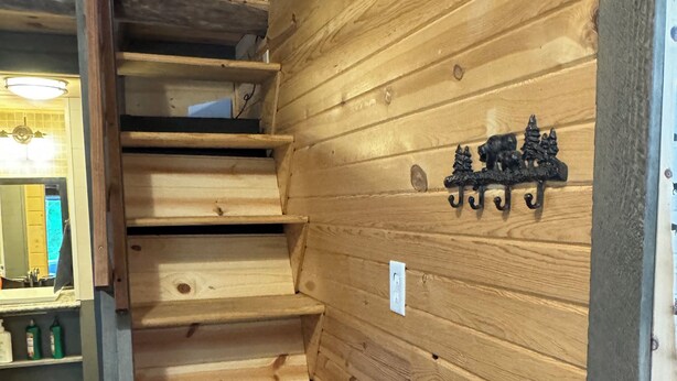 Una escalera de madera con barandilla de metal, un perchero de pared y un enchufe.