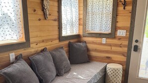 Interior de una cabaña de madera con banca integrada, cortinas estampadas y un adorno de asta de ciervo en la pared.