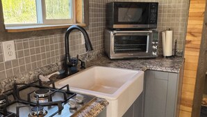 Una cocina compacta con estufa a gas, lavamanos, microondas y ventana.