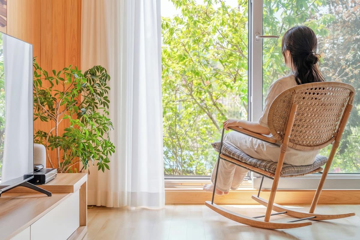 A person sitting on a rocking chair by a window with a view of trees.