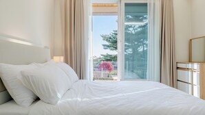 A hotel room with a bed, a bedside table, a mirror, and a view of the outdoors through a glass door. - Gangneung Stay Gaju Gangneung (Gangneung)