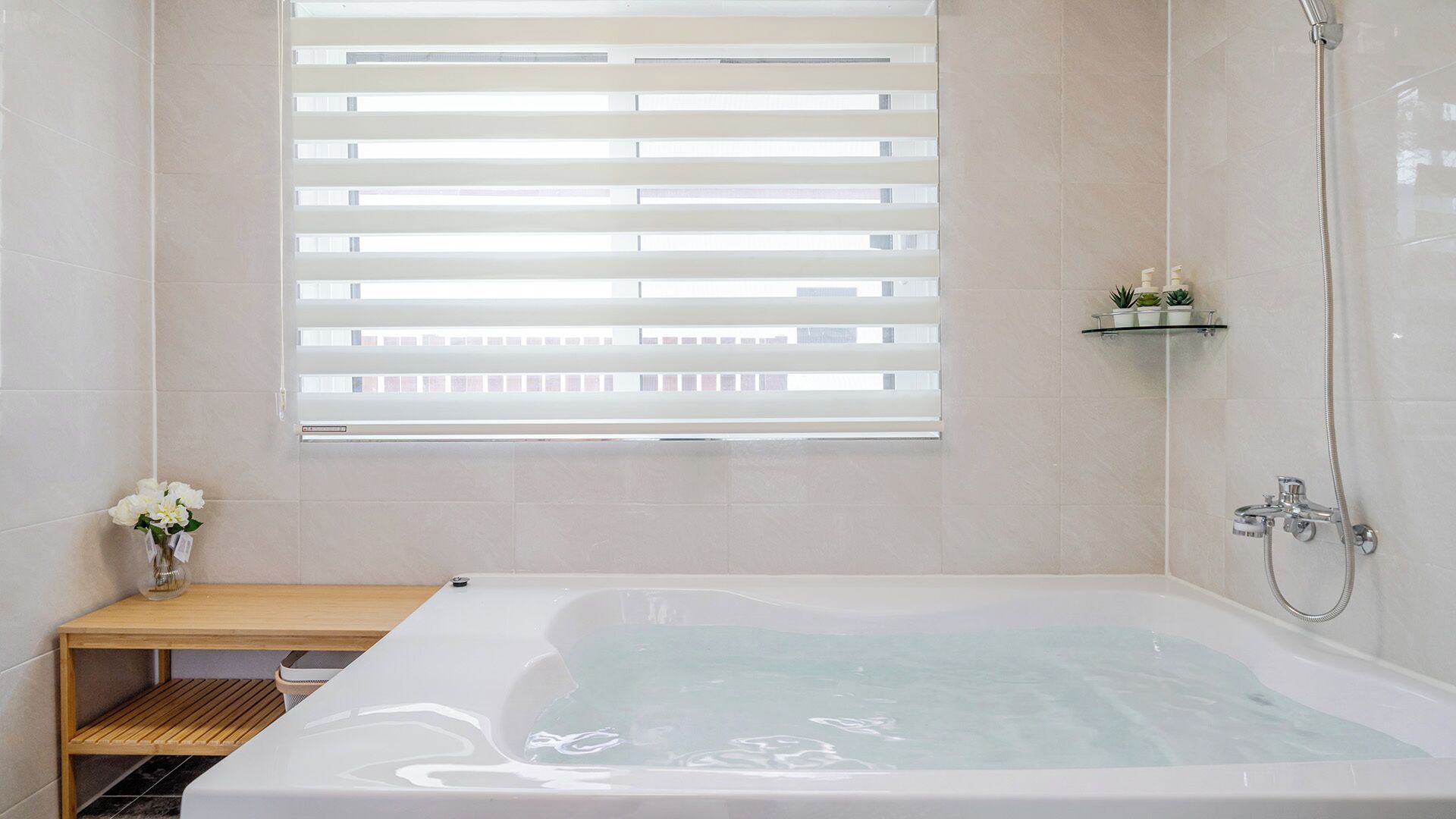 A modern bathroom with a bathtub, shower, and window with blinds.