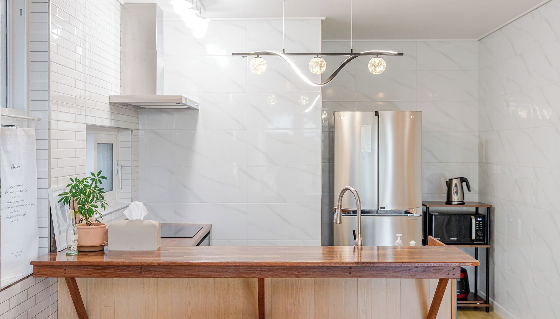 A modern kitchen with a wooden countertop, stainless steel appliances, and a hanging light fixture.