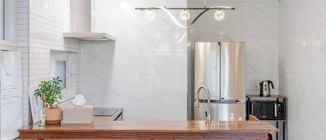 A modern kitchen with a wooden countertop, stainless steel appliances, and a hanging light fixture.