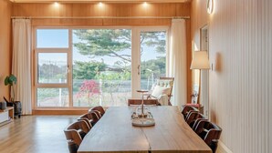 A spacious room with a large wooden table, multiple chairs, a sofa, and a view through large windows. - Gangneung Stay Gaju Gangneung (Gangneung)