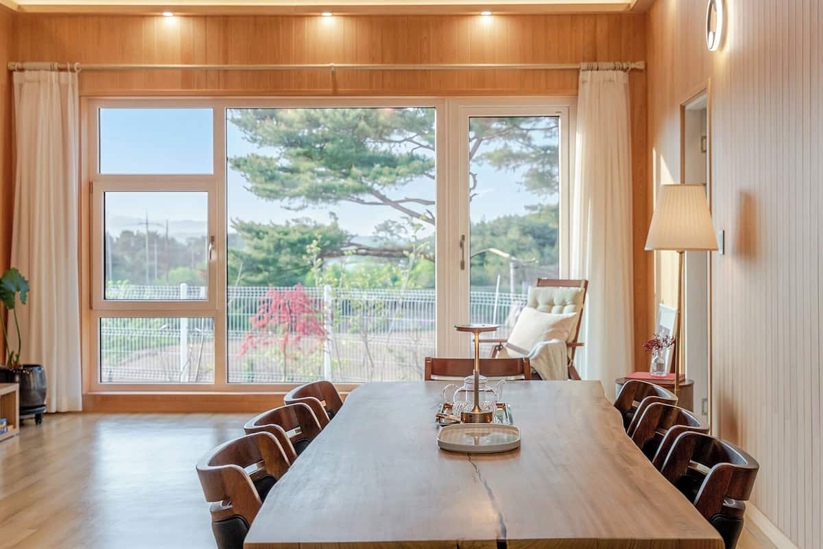 A spacious room with a large wooden table, multiple chairs, a sofa, and a view through large windows.