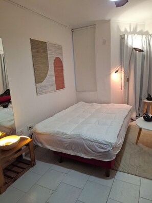 A bedroom with a bed, a bedside table with a lamp, a mirror, and a wall-mounted artwork.