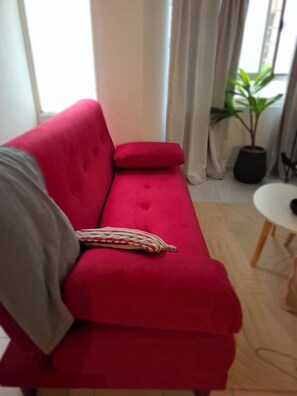 A red sofa with a striped pillow, a grey blanket, and a potted plant in a corner.