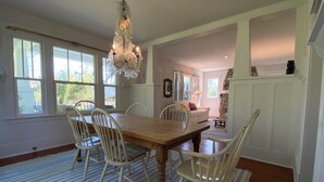 Un comedor con una mesa y sillas de madera, una lámpara de araña y ventanas amplias.
