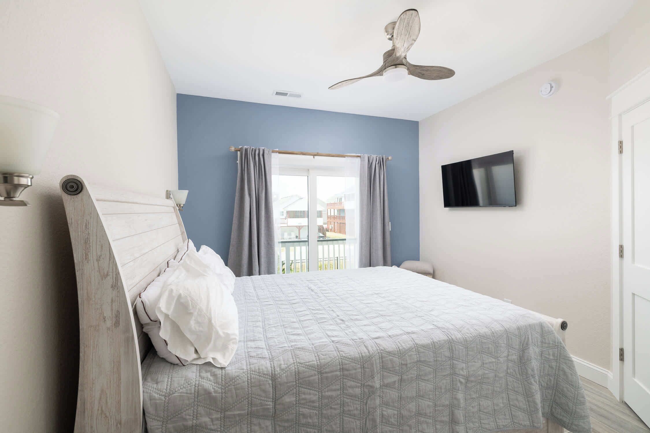 A bedroom with a bed, a ceiling fan, a TV, and a balcony view.
