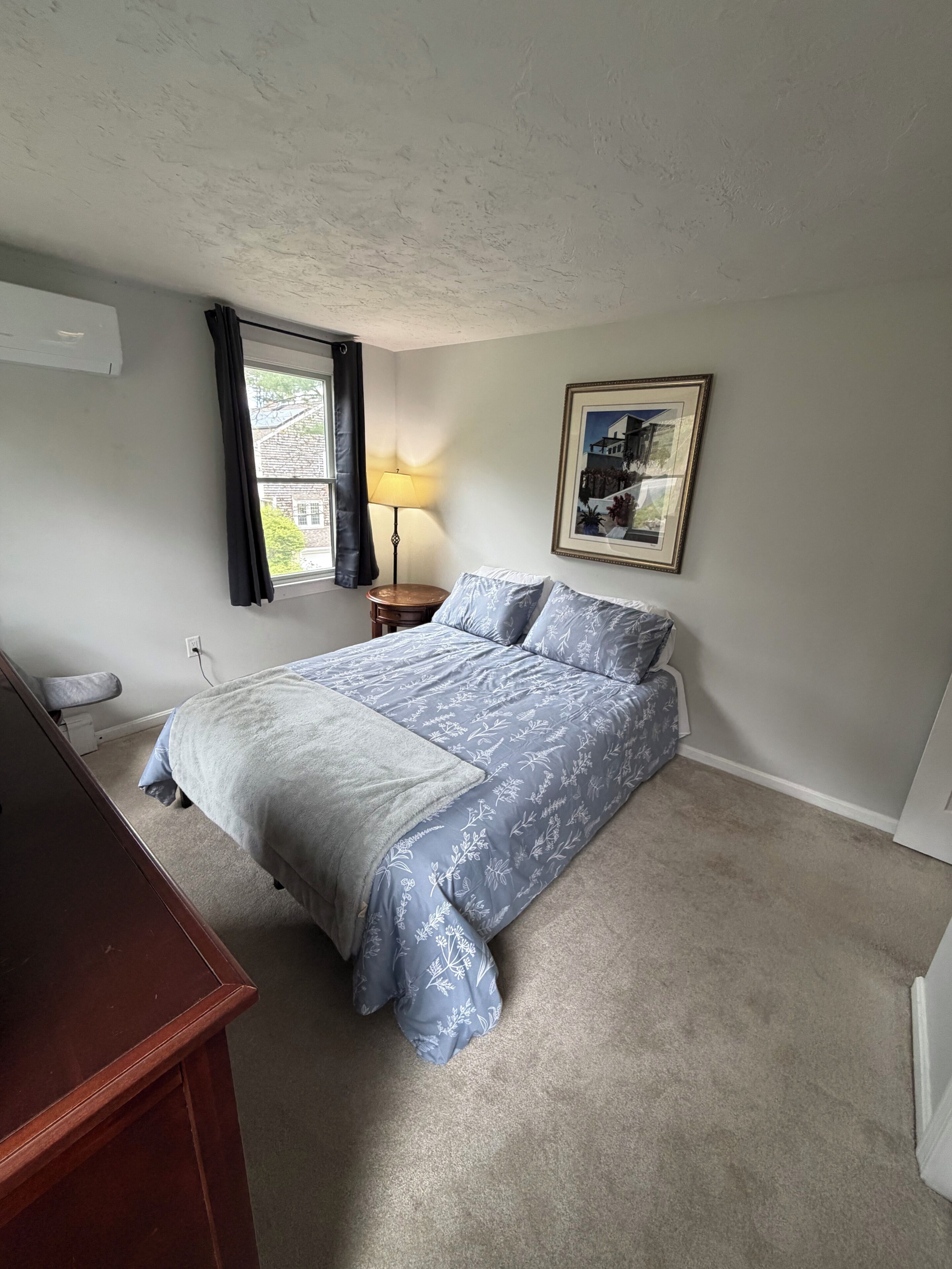 Un dormitorio con cama, escritorio, lámpara y un cuadro en la pared.