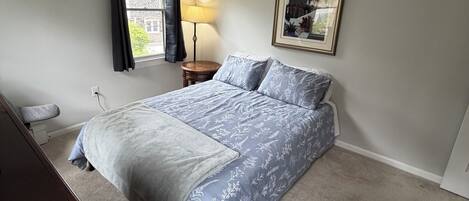 Un dormitorio con cama, escritorio, lámpara y un cuadro en la pared.