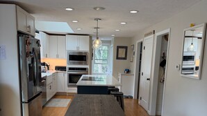 A modern kitchen with a central island, wooden flooring, and built-in appliances. - Short drive to local beaches. Levitate Festival’s less than a mile and walkable  (Marshfield)