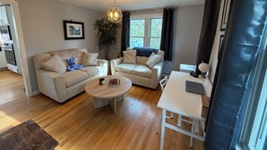 A modern living room with two sofas, a coffee table, a dining table, a potted plant, and a hanging light fixture. - Short drive to local beaches. Levitate Festival’s less than a mile and walkable  (Marshfield)
