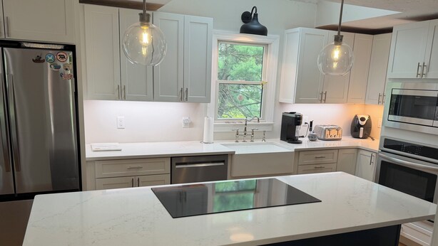 A modern kitchen with white cabinets, a stainless steel refrigerator, a black island, pendant lights, and a window with a view of trees. - Short drive to local beaches. Levitate Festival’s less than a mile and walkable  (Marshfield)