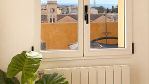 A room with a window overlooking a cityscape, a radiator below, and an air conditioning unit above.