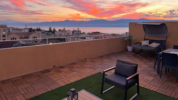 A rooftop terrace with a view of the sea and mountains, a covered seating area, and a small table.