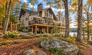 A two-story house with a balcony, surrounded by trees and a lake.