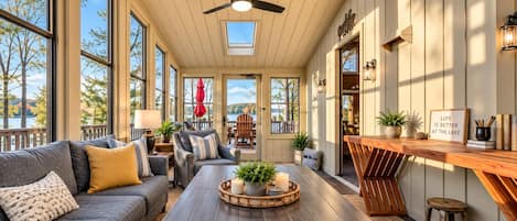 Un interior acogedor con ventilador de techo de madera, ventanas amplias, zona de comedor con mesa de madera y vistas al exterior.