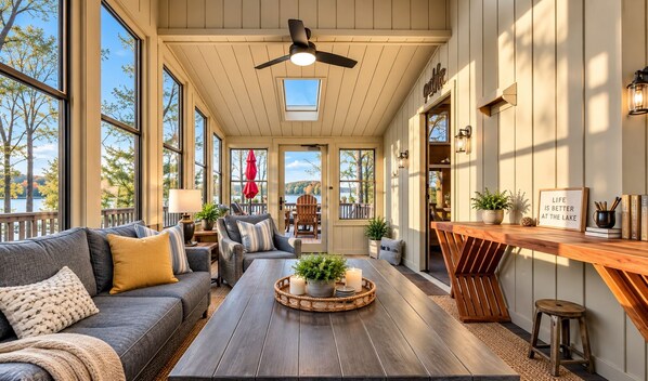 A cozy interior with a wooden ceiling fan, large windows, a dining area with a wooden table, and a view of the outdoors.