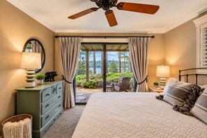 A bedroom with a bed, a dresser, a mirror, a ceiling fan, and a view of a garden through a sliding door.
