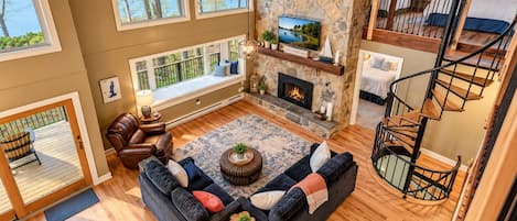 Un salón espacioso con chimenea, un ventanal grande con vistas a un lago y una escalera de madera.