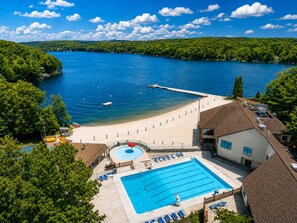 A resort with a swimming pool, beach area, and a view of a lake.