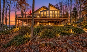 A modern house with a large deck, surrounded by trees and a forested landscape.