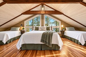 A bedroom with two beds, a large window, wooden beams, and a view of trees.