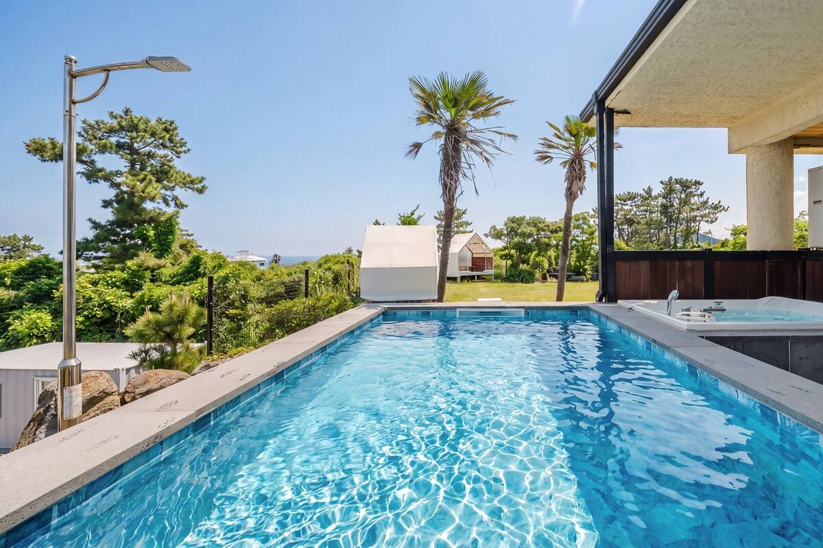 A swimming pool with a hot tub, surrounded by palm trees and a view of the ocean.
