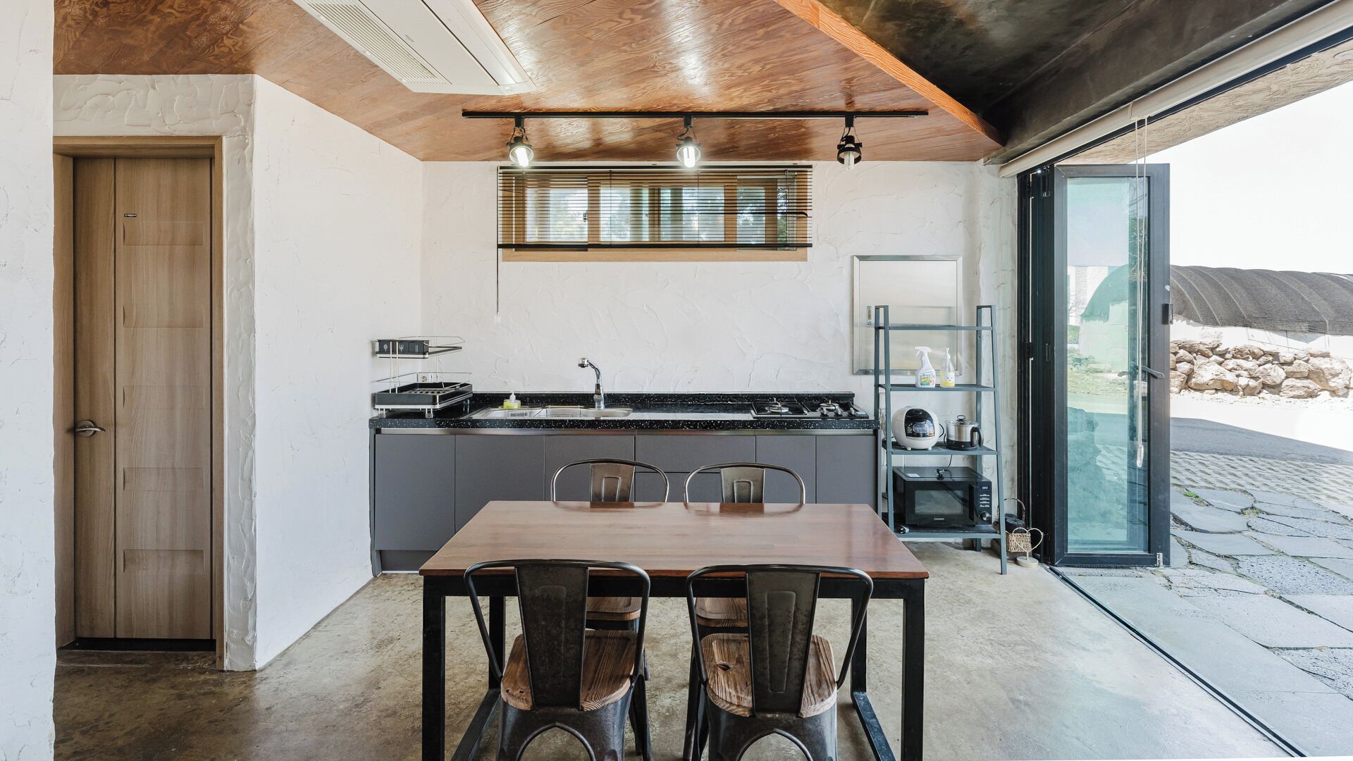 Eine moderne Küche mit Essbereich, ausgestattet mit einem Holztisch und -stühlen, einem eingebauten Backofen und Blick durch eine Glastür.