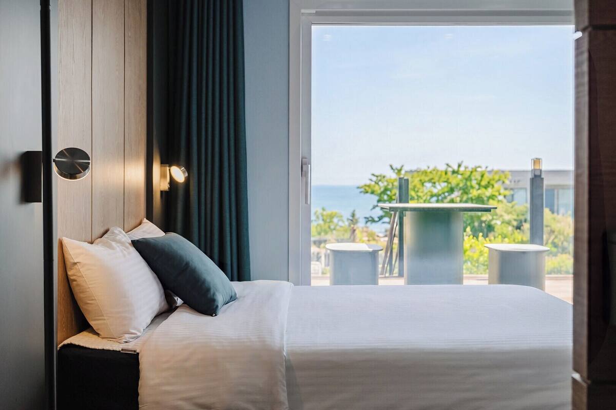 A hotel room with a bed, a view of the outdoors, and a table outside.