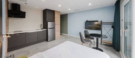 Una habitación de hotel moderna con cama, kitchenette, zona de comedor y un ventanal grande.