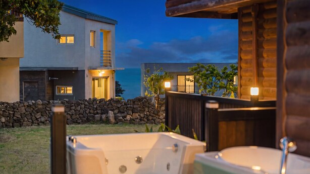 Ett modernt hus med en stenmur, ett trädäck och en jacuzzi.