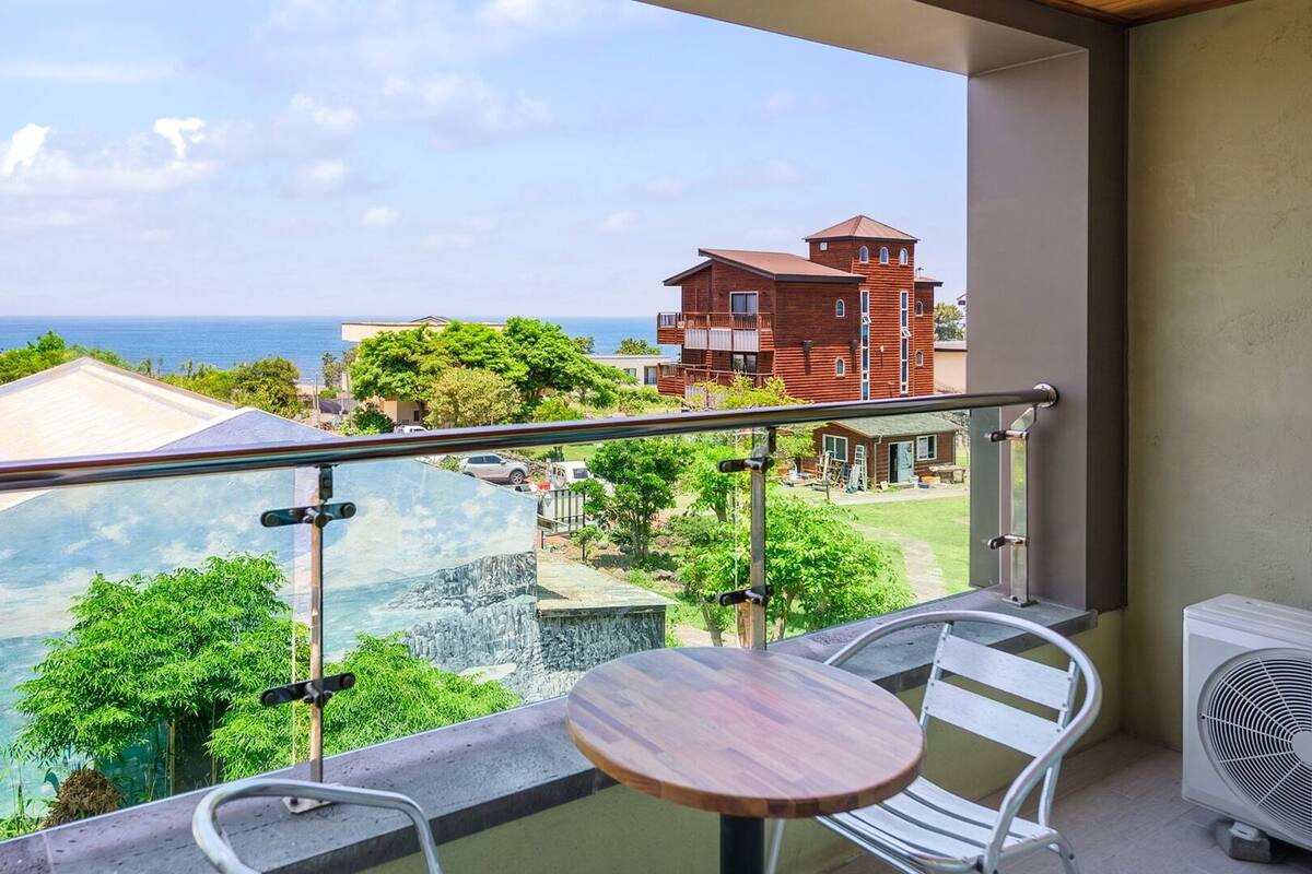 A balcony with a view of the sea, a table, chairs, and an air conditioning unit.