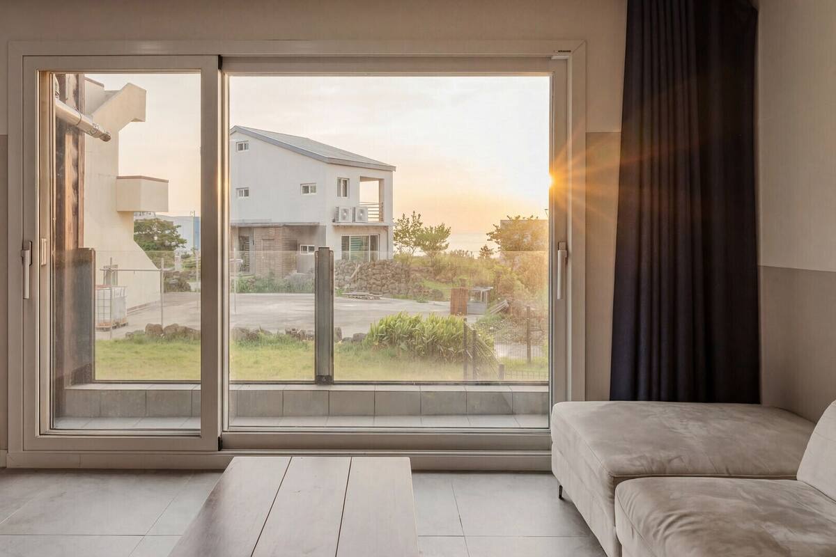 A modern room with a sliding glass door leading to a balcony, a beige sofa, and a view of a residential area.