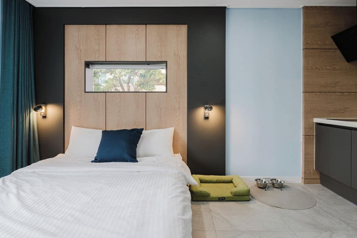 A modern hotel room with a bed, a small window, and a kitchenette area.