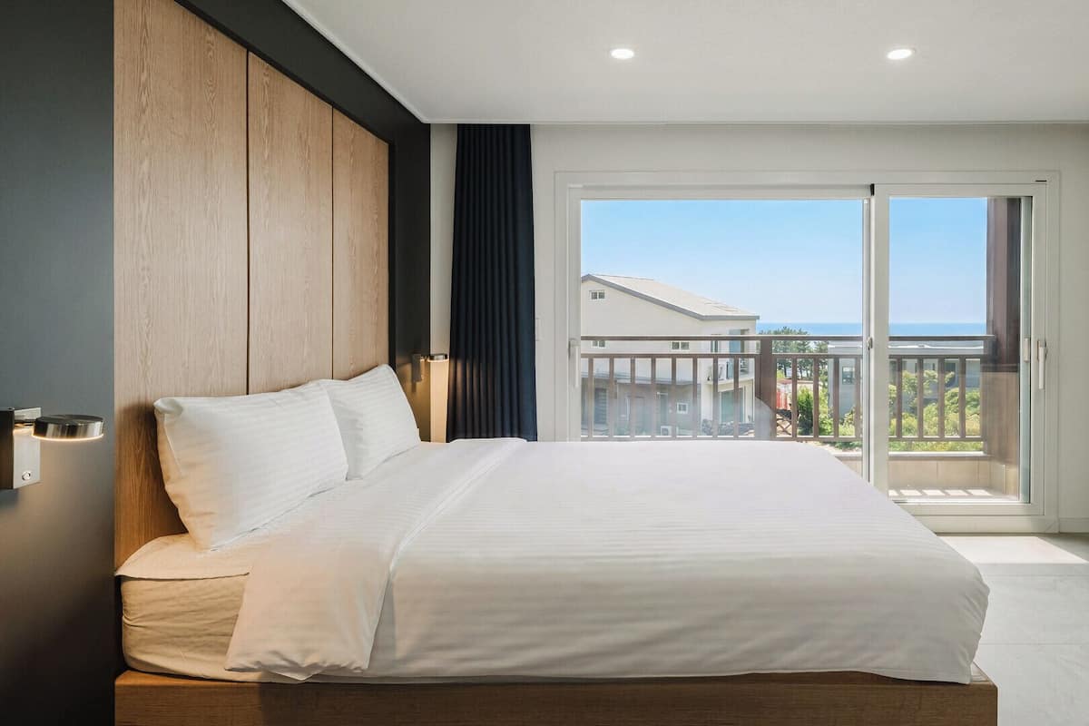 A bedroom with a large bed, a wooden headboard, a balcony with a view, and a sliding glass door.