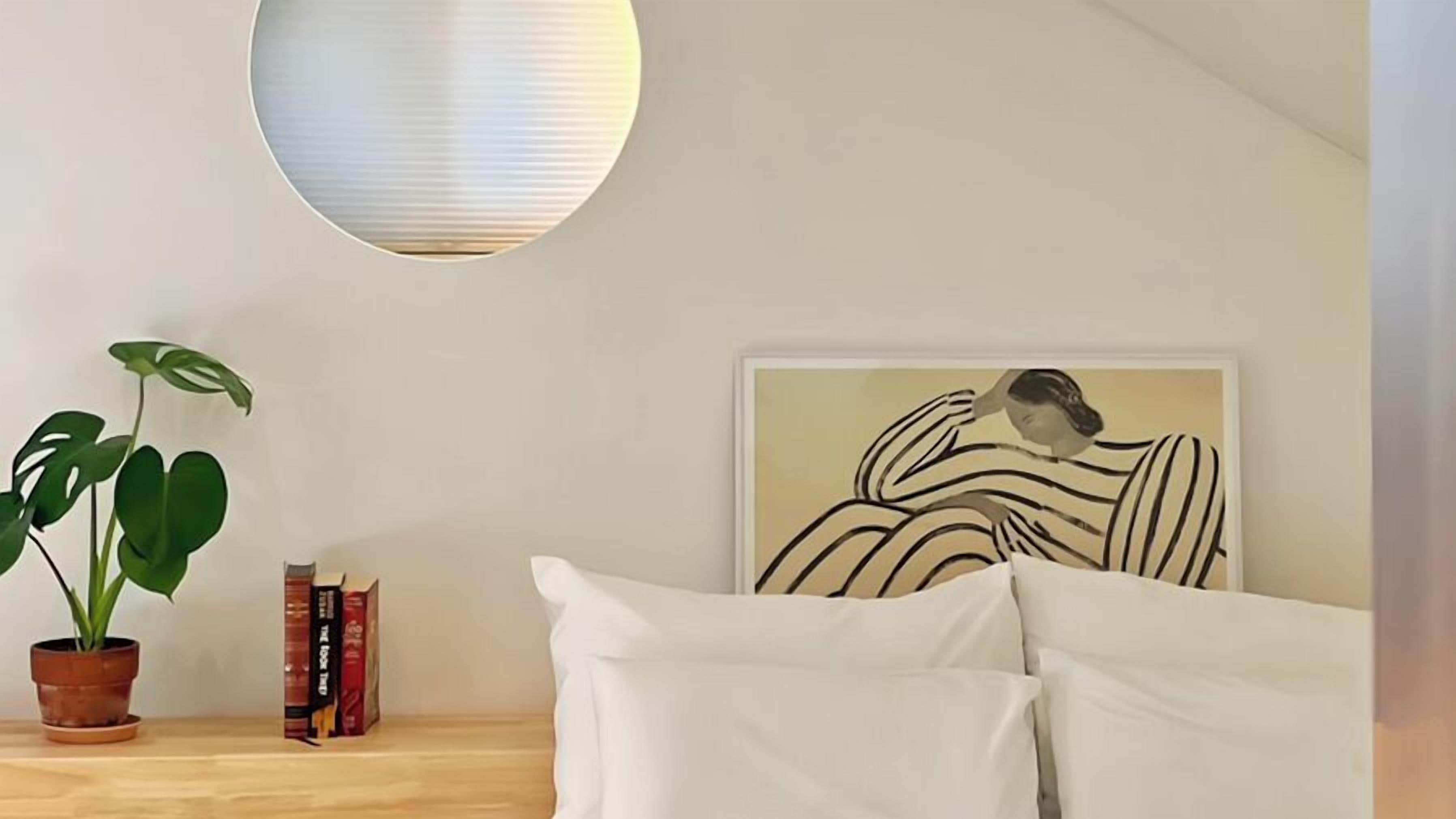 Ein Schlafzimmer mit einem Bett, einer Topfpflanze, einer Wandleuchte und einem gerahmten Kunstwerk.